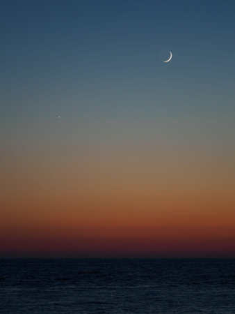 Orange and blue sunset in the sea. The moon in the form of a crescent over the water.