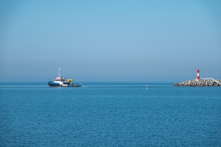 The sea tug comes out of the harbor next to the lighthouse. Sea harbor on a sunny day.の写真素材