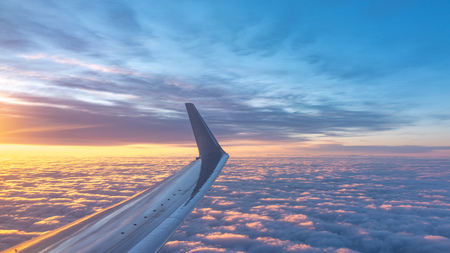 Beautiful salmon dawn and the wing of an airplane above the clouds. View of the dawn in the clouds from the plane. Airplane flying above clouds at pink sunriseの写真素材