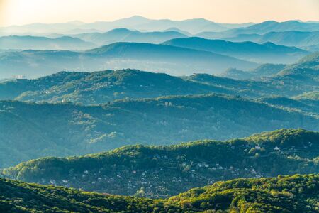 Layers of green mountains and hills in the haze during sunset. Beautiful sunset in the mountains. Beautiful sunset in a hilly valley with villages and fog in the lowlands.の写真素材
