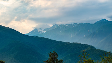 Mountain ranges with green and rocky slopes. Mountains with snowy peaks hidden in the clouds. Thick...