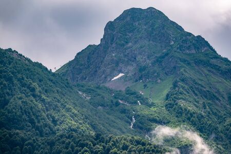Green slopes and rocky peaks of high mountains in cloudy summer day. Summer or spring in the mountains.の写真素材