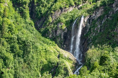 Views of the green mountains with rocks and the highest waterfall. Powerful stream of a mountain river among stones and rocks.の写真素材