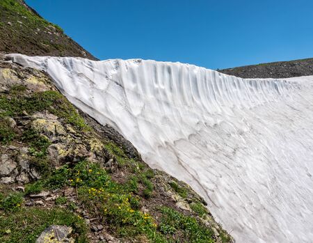 Mountain range with rocks and snow on slopes against a clear blue sky. Mountain peak in the summer.の写真素材