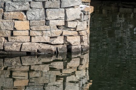 Stonework of a bridge pylon with reflection in the water. Old stone bridge and a riverの写真素材