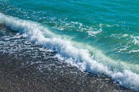 Sea wave with foam on a pebble beach. Wet bright shining different colored pebble stones and sea foamの写真素材