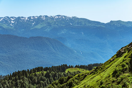 Green mountain ridges, surrounded by high mountains. Snow-capped mountain peaks on the horizon....