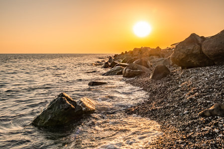 Orange sunset on the seashore with large stones. Large stones with beautiful texture on the background of dawn on the sea. Evening landscape rocky shoreの写真素材
