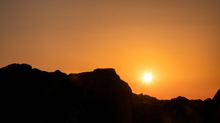 Sunset in the orange sky. Amazing Sunset or Sunrise With Sun Over Dark Mountain Silhouette. Sunset in the orange skyの写真素材