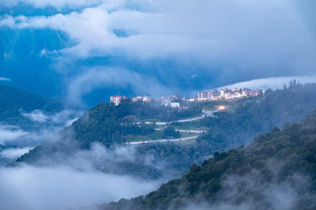 The complex of hotels in the mountains among the green forest. Beautiful clouds and heavy fog at...