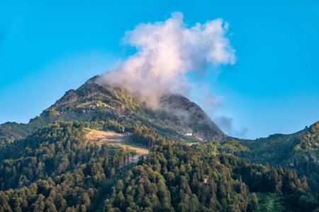 Green mountain slope with cable cars and ski runs at clear summer sunset. Black Pyramid Mountain,...