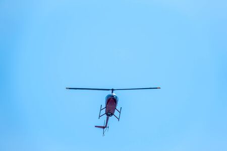 A small two seater commercial helicopter set against a clear, blue sky passes from bottom to top. A small helicopter flies in a clear blue sky.の写真素材