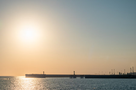 Clear sky and bright sunset at sea port with a breakwater and a lighthouse. Copy space background