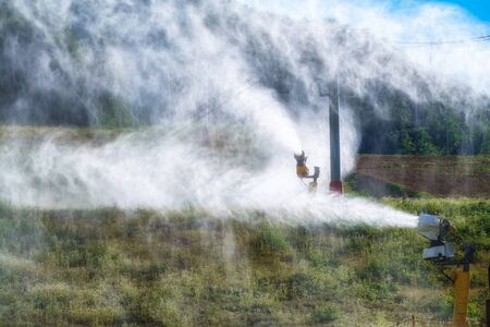 Snow gun in the summer in the mountain ski resort. A hillside snowmaker works in summer for prevention. Snow machine works in the summer.の写真素材