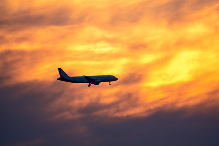 Airplane landing on orange cloudy dramatic sunset. Airplane landing against setting sun. Travel...