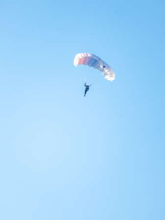 One parachutist with white parachute floats slowly at low altitude on the background of clear sky. Skydiving, sports and active kind of extreme relaxationの写真素材