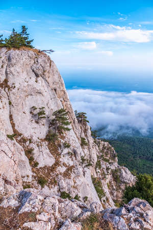 A majestic view of the rocky mountains and the valley in fog and clouds. Creamy fog covered the mountain valley in sunset light. Misty sunset over Crimea Mountains. Location place Ai-Petri, Crimea.の写真素材