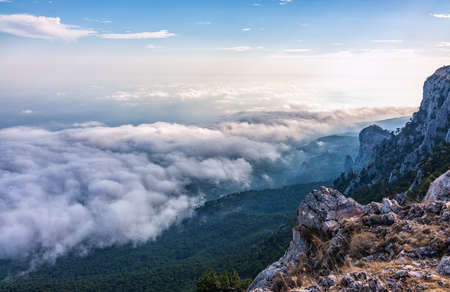 A majestic view of the rocky mountains and the valley in fog and clouds. Creamy fog covered the mountain valley in sunset light. Misty sunset over Crimea Mountains. Location place Ai-Petri, Crimea.の写真素材