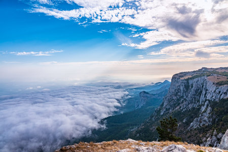 A majestic view of the rocky mountains and the valley in fog and clouds. Creamy fog covered the mountain valley in sunset light. Misty sunset over Crimea Mountains. Location place Ai-Petri, Crimea.の写真素材