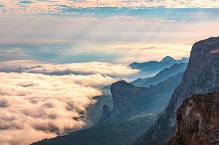 A majestic view of the rocky mountains and the valley in fog and clouds. Creamy fog covered the...