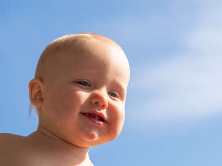 Happy baby in mother's arms against the blue sky. Cute baby in her mother arms outdoors portrait. Mom holds the baby on a blue background. Mother's day conceptの写真素材