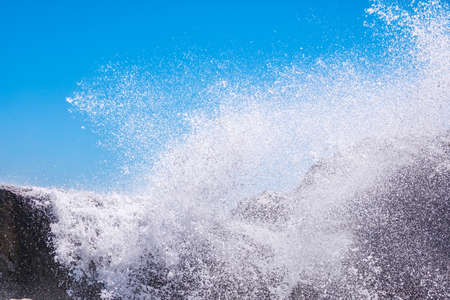 Sea water beats against rocks. Sea waves of dark water beat against the coastal rocks. An infinite number of splashes, drops of water and white foam are scattered.の写真素材