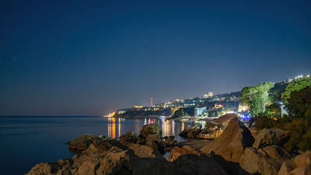 Green sea shore with residential buildings in the night. Seascape with clear sky at night.の写真素材