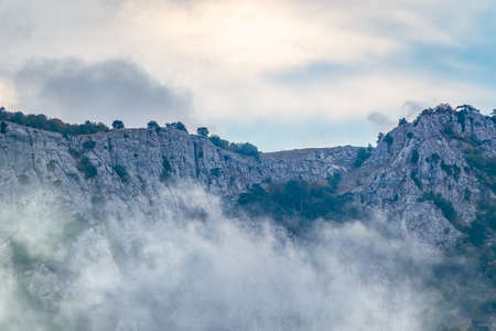 High rocky mountains with forested slopes and peaks hidden in the clouds. Heavy fog in the mountains on a cloudy day. Ai-Petri, Crimeaの写真素材