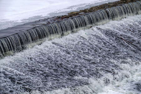 A small flat cascade in a calm river with ice in winter. Water backgroundの写真素材