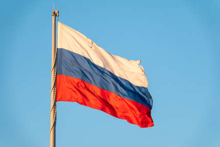 Russian tricolor flag waving in the wind against a blue sky. Russian flag on blue backgroundの写真素材