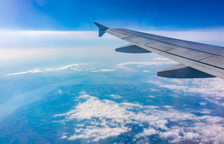 View from the airplane window at a beautiful cloudy sky and the airplane wing. Earth and sky as seen through window of an airplane.の写真素材