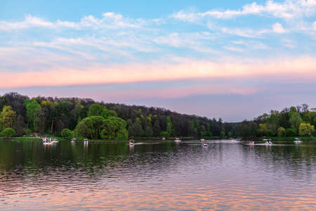 A pond in the Tsaritsino city park on a summer evening with people sailing on boats. A summer landscape on a pond with floating boats in the warm summer evening. Moscow, Russiaの写真素材