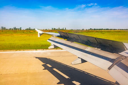 View of airplane wing, blue skies and green land with plane shadow during landing. Airplane window view. Earth and sky as seen through window of an airplane.の写真素材