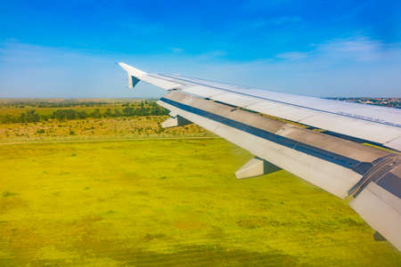 View of airplane wing, blue skies and green land during landing. Airplane window view. Earth and sky as seen through window of an airplane.の写真素材
