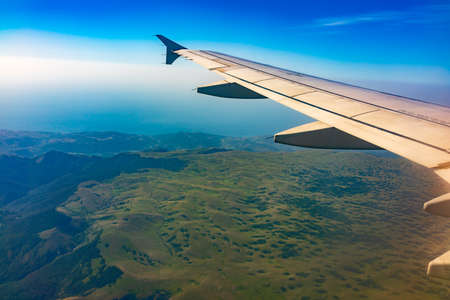 View of airplane wing, blue skies and green land during landing. Airplane window view. Earth and sky as seen through window of an airplane.の写真素材