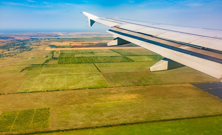 View of airplane wing, blue skies and green land during landing. Airplane window view. Earth and sky as seen through window of an airplane.の写真素材