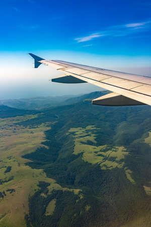 View of airplane wing, blue skies and green land during landing. Airplane window view. Earth and sky as seen through window of an airplane.の写真素材
