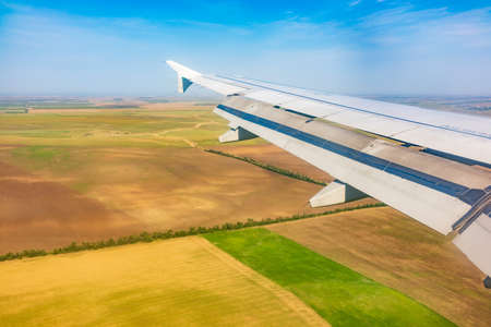 View of airplane wing, blue skies and green land during landing. Airplane window view. Earth and sky as seen through window of an airplane.の写真素材