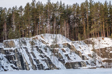 Sheer cliffs and rocks around the Talc quarry in winter in Russia in the town of Sysert, near Yekaterinburg. Pine and birch on a snow-covered rockの写真素材