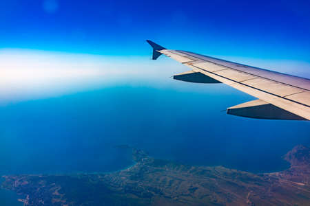 View from the airplane window at a beautiful blue clear sky, earth, sea and the airplane wing. Earth, sea and sky as seen through window of an airplane.の写真素材