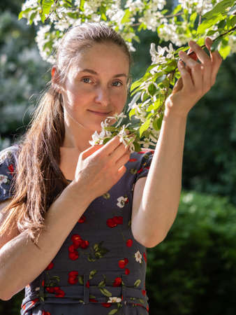 Beautiful Young woman without makeup in a spring park flowering among trees. Close-up portrait of a natural girl without makeup with tilted the head over a green background. Spring is coming.の写真素材