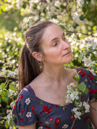 Beautiful Young woman without makeup in a spring park flowering among trees. Close-up portrait of a natural girl without makeup with tilted the head over a green background. Spring is coming.の写真素材