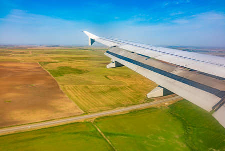 View of airplane wing, blue skies and green land during landing. Airplane window view. Earth and sky as seen through window of an airplane.の写真素材