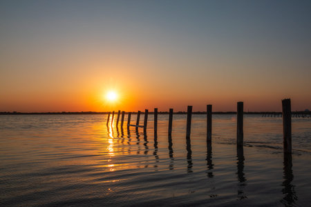 Beautiful red and orange sunset over sea, the sun goes down over sea. Dramatic Sunset Sky. A flock of cormorants sits on old sea pier in orange sunset light. The great cormorant, Phalacrocorax carboの写真素材