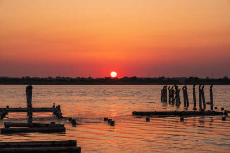 Beautiful red and orange sunset over sea, the sun goes down over sea. Dramatic Sunset Sky. A flock of cormorants sits on old sea pier in orange sunset light. The great cormorant, Phalacrocorax carboの写真素材