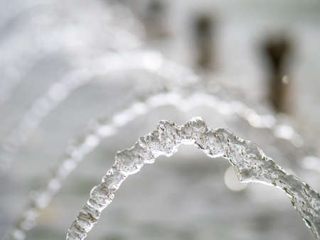 Splashes of water against light background. Fountain, a jet of water against cloudy sky.の写真素材