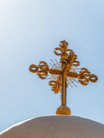 Christian cross on a mound against a blue sky with white clouds. Christian symbol. Religion and culture. Catholicism and Protestantism. Place of crucifixion. Easter. Cross against blue skyの写真素材