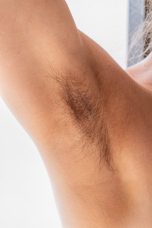 Closeup of long dark hair growing under arm of young female. Concept of hygiene, Female hairy armpit, unshaved underarms new fashion trend concept. Feminism, Beauty standards, skin, body care conceptの写真素材