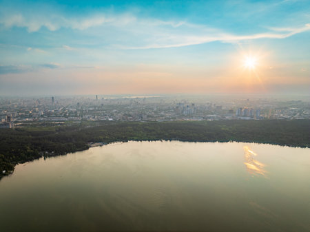 Big lake with green shores in bright sun light and city on horizon, aerial landscape. Recreation concept. Sky reflection. Aerial view.の写真素材