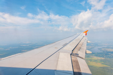 View of airplane wing, blue skies and green land during landing. Airplane window view. Earth and sky...